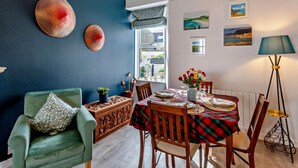 Un coin repas avec une table dressée pour deux personnes, un fauteuil vert et une fenêtre donnant sur un beau paysage.