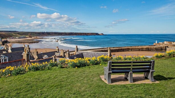 Une vue sur la côte, avec un banc, un ciel dégagé et une ligne de rivage lointaine.