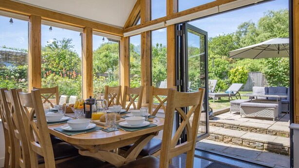 A dining area with wooden chairs and tables, large windows, and a view of the garden. - 5 Bed in Telford (oc-72844) (New Works)