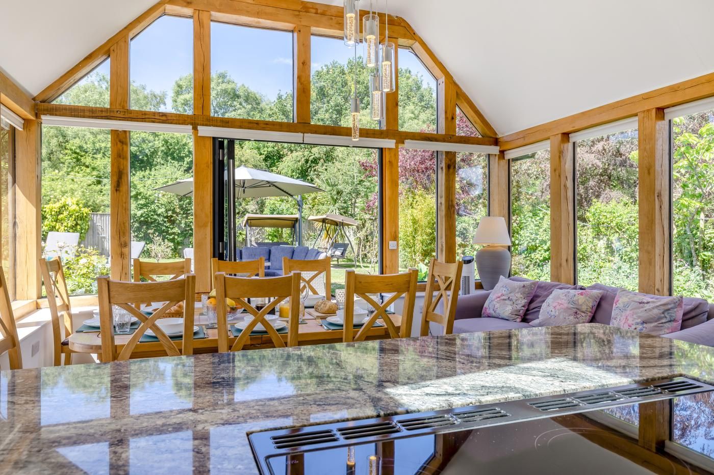 A spacious room with a large dining table, wooden chairs, a sofa, and a view of the outdoors through large windows.