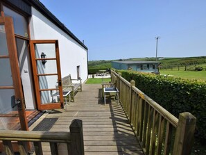 A wooden deck leading to a white building with a glass door, a bench, and a table. - 4 Bed in Bideford (oc-owlbr) (Higher Clovelly)