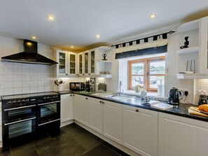 A modern kitchen with white cabinetry, a black stove, and a window with a view of the outside. - 4 Bed in Bideford (oc-owlbr) (Higher Clovelly)