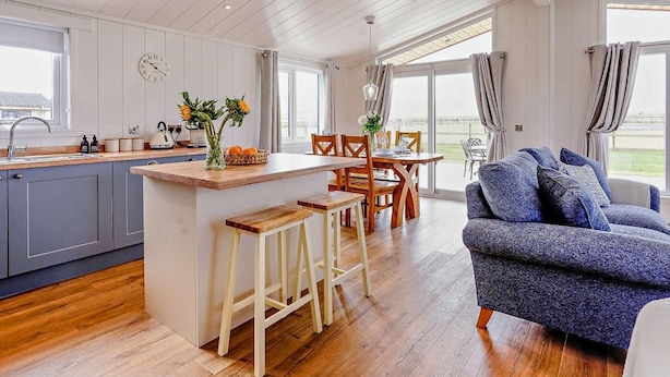 A modern kitchen with a central island, wooden flooring, a dining area with chairs, and a sofa with cushions. - 2 Bed in St. Andrews (oc-93228) (St Andrews)