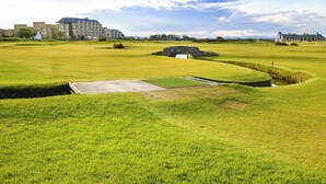 A golf course with a bridge, a pond, and buildings in the background. - 2 Bed in St. Andrews (oc-93228) (St Andrews)