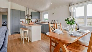 A modern kitchen with grey cabinets, a central island, wooden stools, and a dining area with a table set for four. - 2 Bed in St. Andrews (oc-93228) (St Andrews)