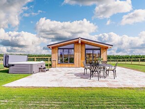 Ein modernes Holzhaus mit Terrasse, Sitzgelegenheit im Freien und einem großen Fenster.