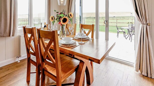 A dining area with a wooden table set for four, large windows, and a view of a tennis court. - 2 Bed in St. Andrews (oc-93229) (St Andrews)