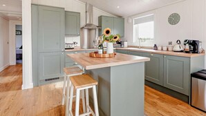 A modern kitchen with a central island, bar stools, a built-in stove, and a large window. - 2 Bed in St. Andrews (oc-93229) (St Andrews)