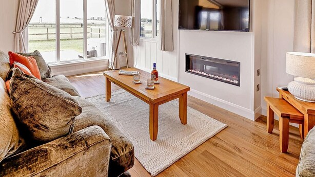 A living room with a wooden coffee table, a sofa, a fireplace, and a TV mounted on the wall. - 2 Bed in St. Andrews (oc-93230) (St Andrews)