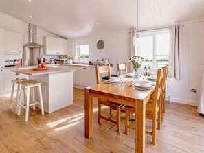 A modern kitchen with a central island, wooden dining table, and chairs. - 2 Bed in St. Andrews (oc-93230) (St Andrews)