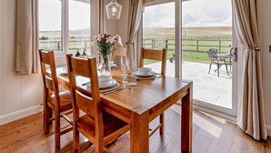 A dining area with a wooden table set for four, large windows, and a view of a grassy field. - 2 Bed in St. Andrews (oc-93230) (St Andrews)