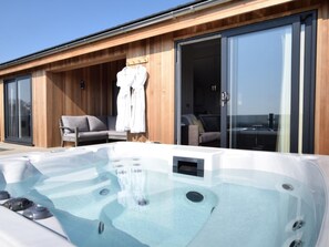 A modern outdoor hot tub with a wooden deck, a sofa, and a sliding glass door leading to an interior space. - 2 Bed in Anstruther (oc-72435) (Anstruther)