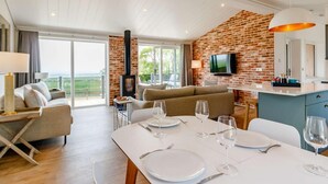 Una sala moderna con chimenea, comedor para dos personas y cocina con pared de ladrillo y televisor.