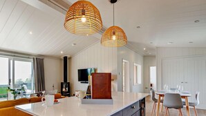 Een moderne keuken met een groot eiland, hanglampen, een inbouwfornuis en een eethoek met een tafel en stoelen.