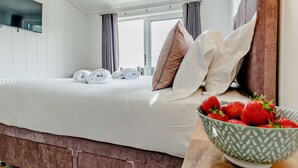 Een hotelkamer met een bed, kussens, een schaal aardbeien en een raam.