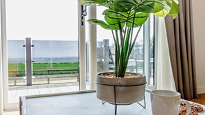 Een balkon met uitzicht op zee, een bloempot, een krant, een mok en een bord met koekjes.
