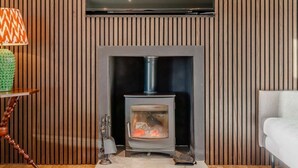A modern living room with a wood-paneled wall, a flat-screen TV mounted above a fireplace, and a cozy seating area. - 2 Bed in Arbroath (oc-84649) (Carmyllie)