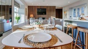 A modern dining area with a round table set for two, a kitchen in the background, and a living area with a TV. - 2 Bed in Arbroath (oc-84649) (Carmyllie)