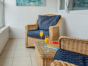 Ein Korbstuhl mit Kissen, ein Glas Orangensaft und ein Buch auf einem kleinen Tisch.