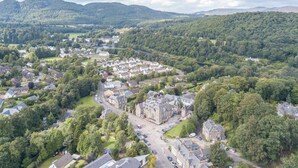 An aerial view of a town with a mix of residential and historical buildings, surrounded by dense forests and hills. - 2 Bed in Birnam, Dunkeld (oc-ca266) (Birnam)