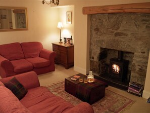 A cozy living room with a stone fireplace, a red sofa, a wooden side table, and a small rug. - 2 Bed in Birnam, Dunkeld (oc-ca266) (Birnam)