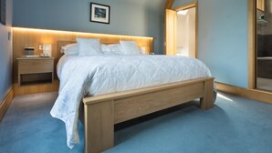 Makuuhuoneessa on puinen sänky, yöpöydät, yölamppu, seinällä oleva kehystetty taulu ja suuri peili.