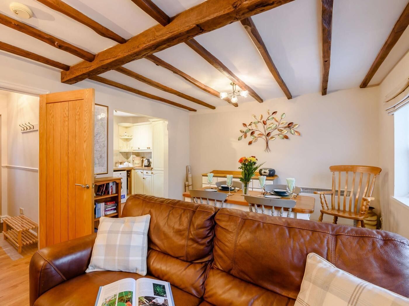 Een gezellige woonkamer met een bruine leren bank, een eethoek met een houten tafel en stoelen, en een keuken op de achtergrond.
