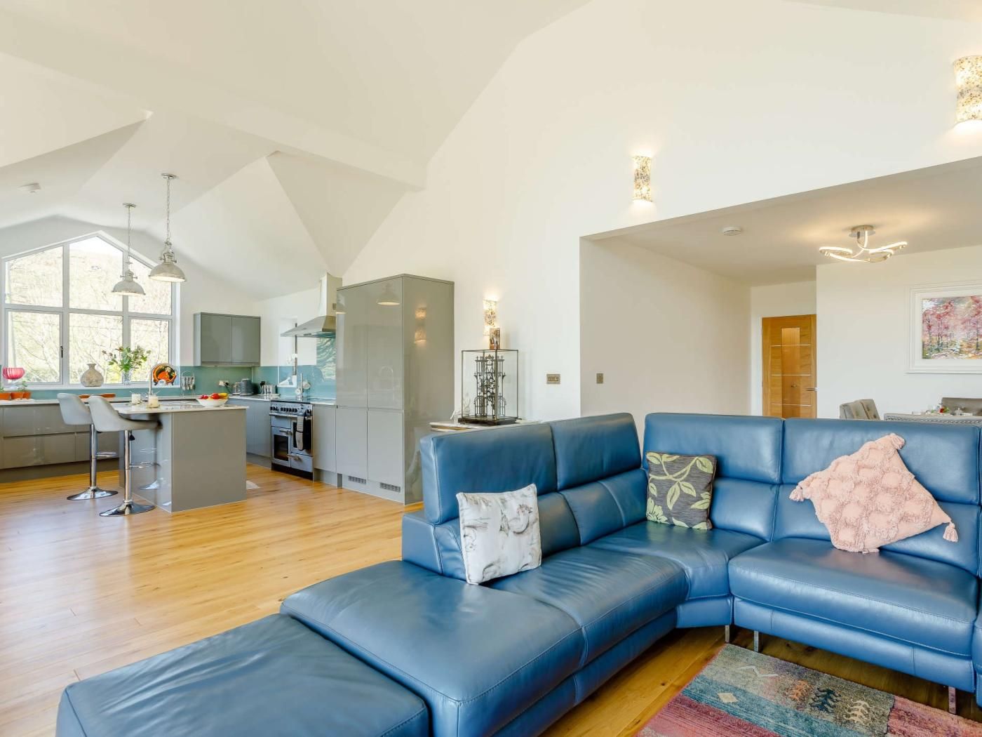 A modern living room with a blue leather sofa, a kitchen with a large island, and a dining area.