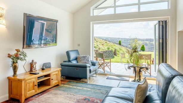 Uma sala de estar ampla com uma janela grande, um sofá azul, um armário de madeira e uma televisão.