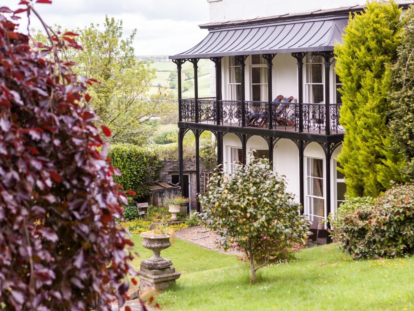 A two-story building with a balcony, surrounded by greenery and a well-maintained garden.