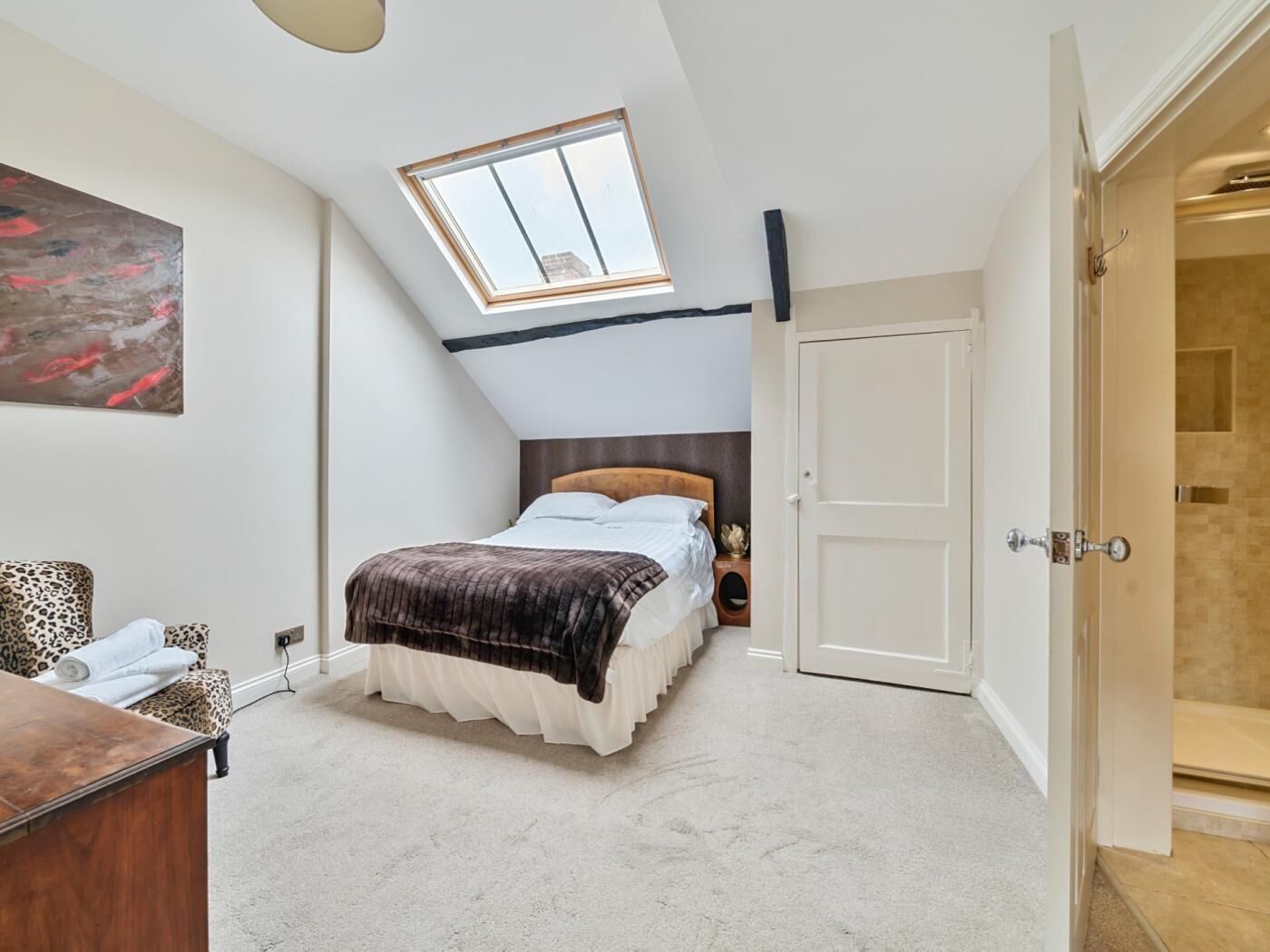 A bedroom with a skylight, a bed with a brown blanket, a leopard-print chair, and a white door.