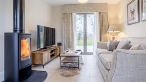 A modern living room with a black wood-burning stove, a flat-screen TV, a sofa, a coffee table, and a lamp. - 2 Bed in Chipping Campden (oc-78128) (Chipping Campden)