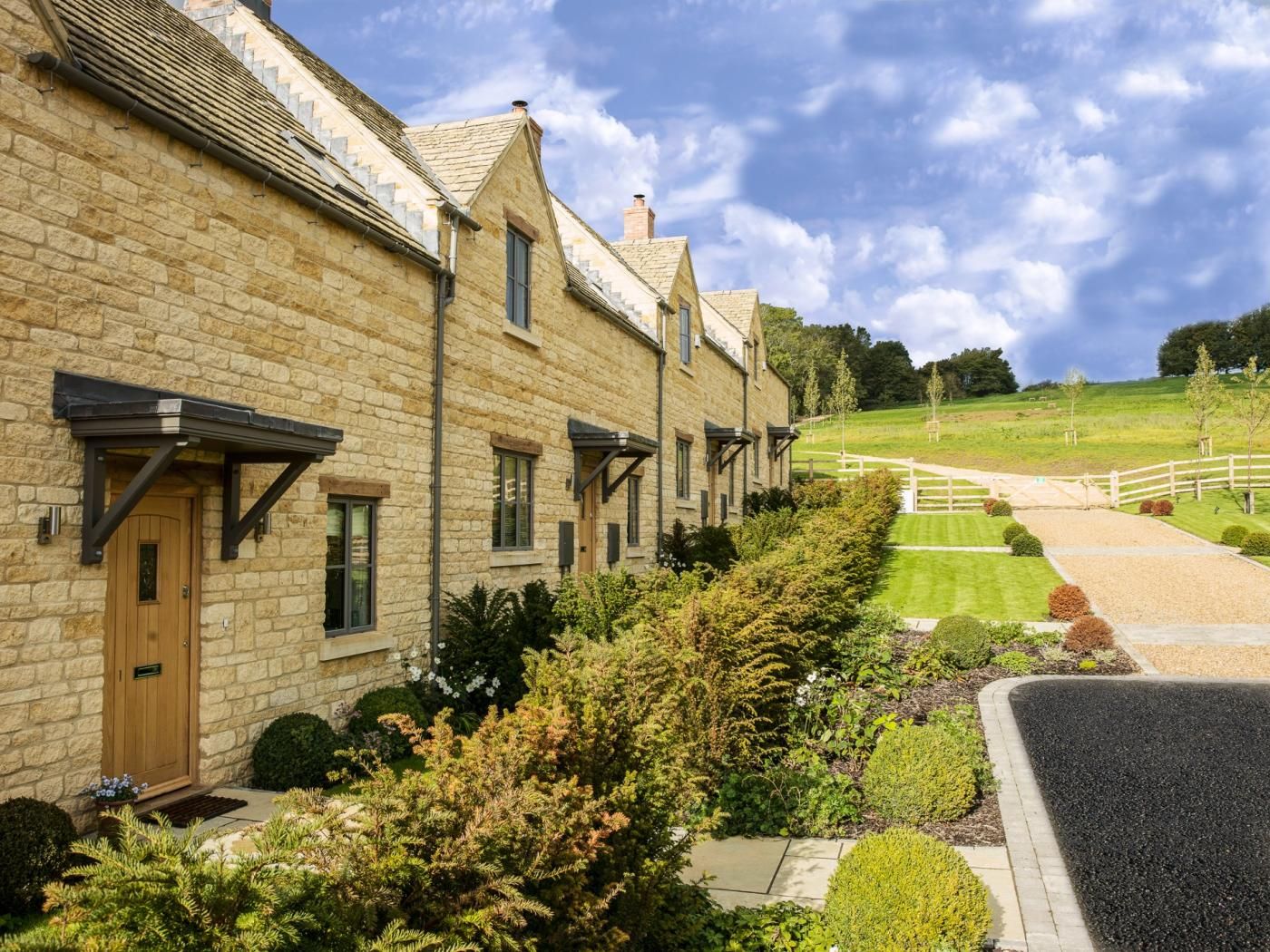 A row of stone buildings with a well-maintained lawn and a gravel path leading to a wooden fence.