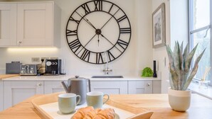 A kitchen with a large wall clock, a coffee maker, and a tray with croissants. - 2 Bed in Chipping Campden (oc-78128) (Chipping Campden)