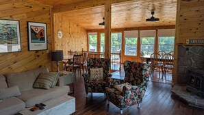 Een houten chalet binnen met een bank, bloemen fauteuils, een eettafel en een stenen open haard.