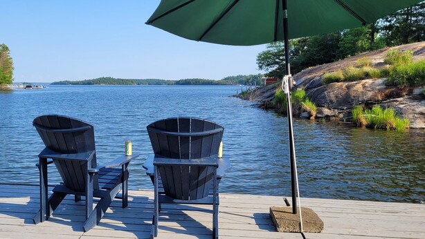 Een houten steiger met twee Adirondack-stoelen en een groene parasol.