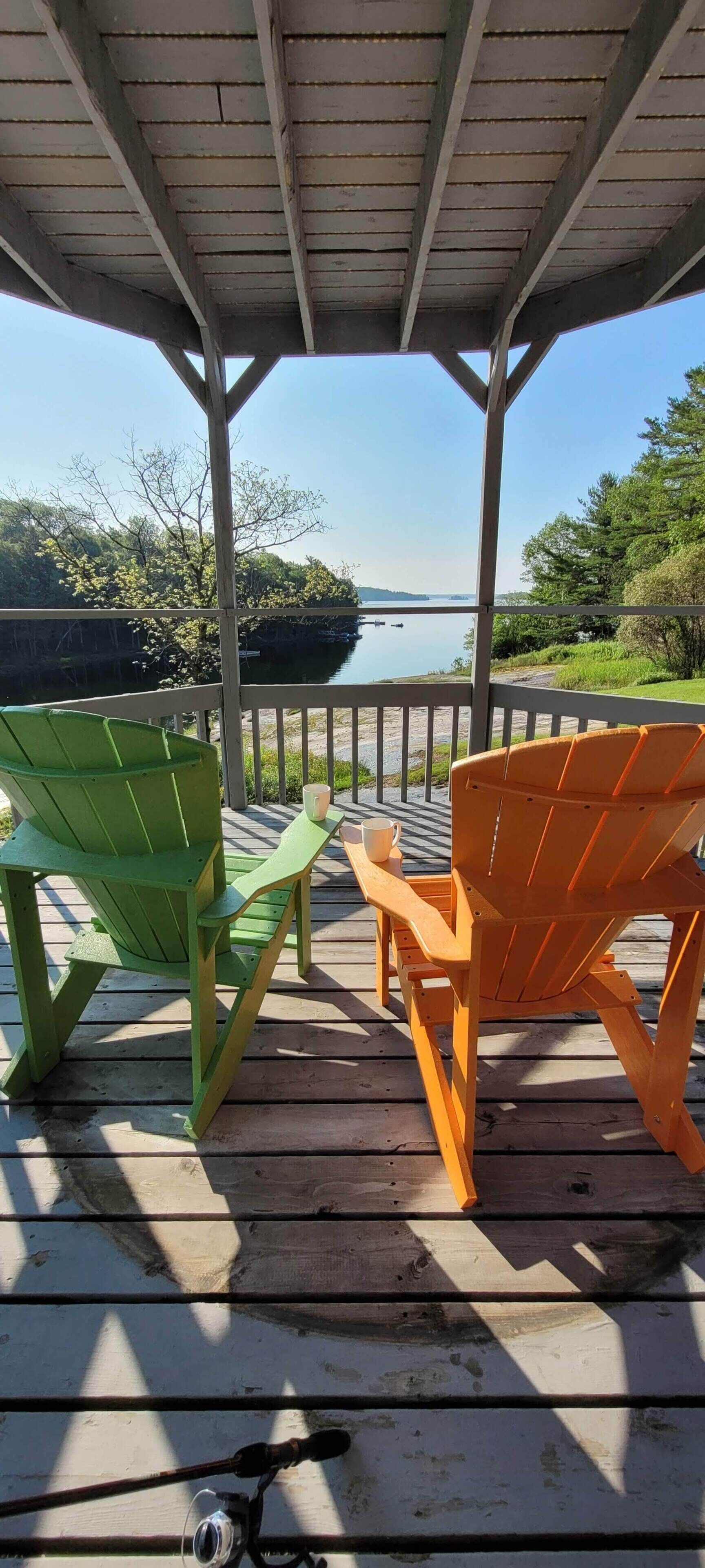 A covered deck with two Adirondack chairs facing a lake.
