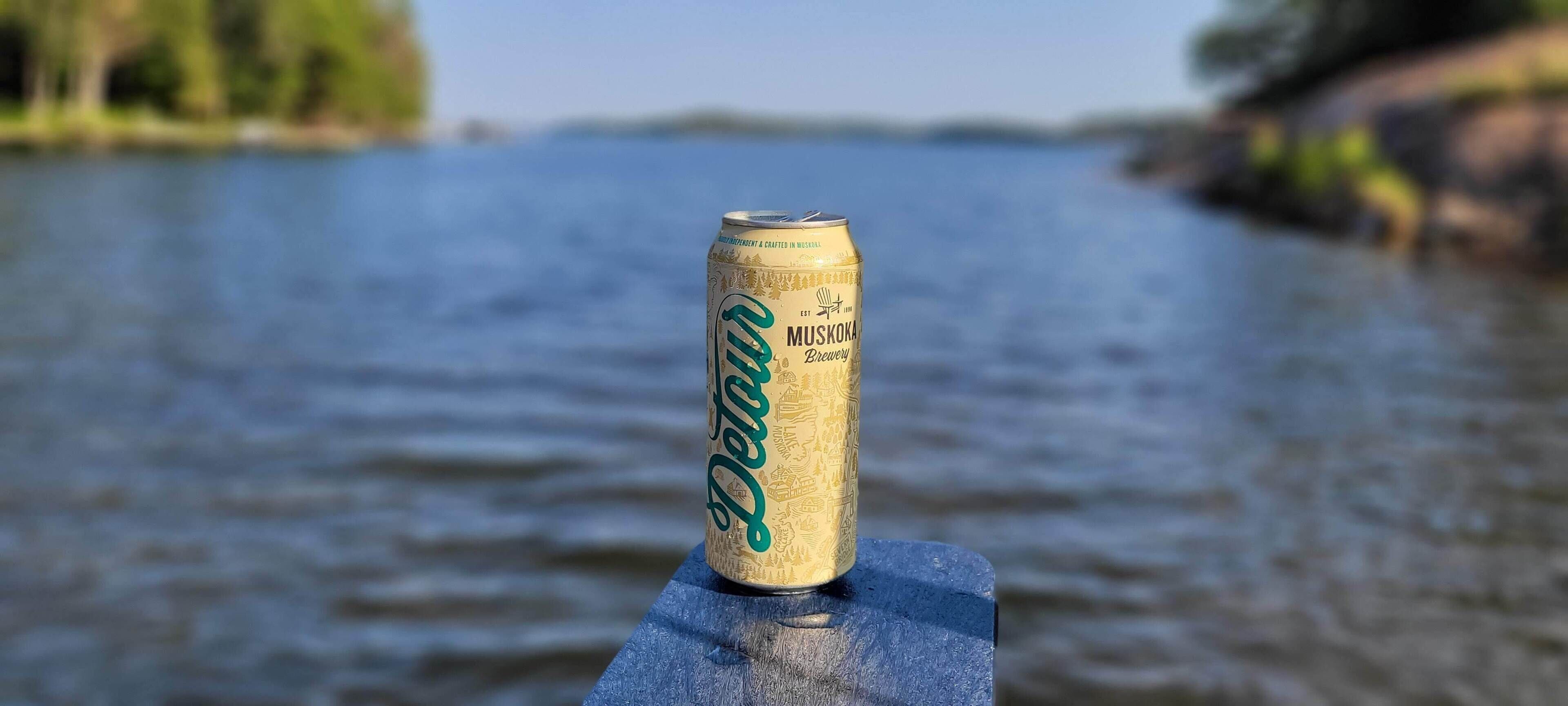 Una llauna de cervesa sobre una superfície de fusta, amb un fons borrat d'aigua i vegetació.