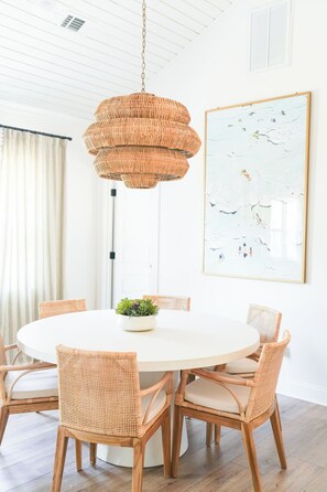 A round dining table with wicker chairs, a hanging wicker chandelier, and a framed abstract painting on the wall. - Eloise Cottage Heated Pool Guest Cottage Golf Cart (St Simons Island)