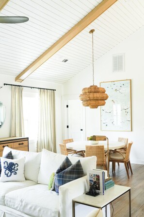A living room with a white sofa, a dining table, wicker chairs, a hanging light fixture, and a framed artwork on the wall. - Eloise Cottage Heated Pool Guest Cottage Golf Cart (St Simons Island)