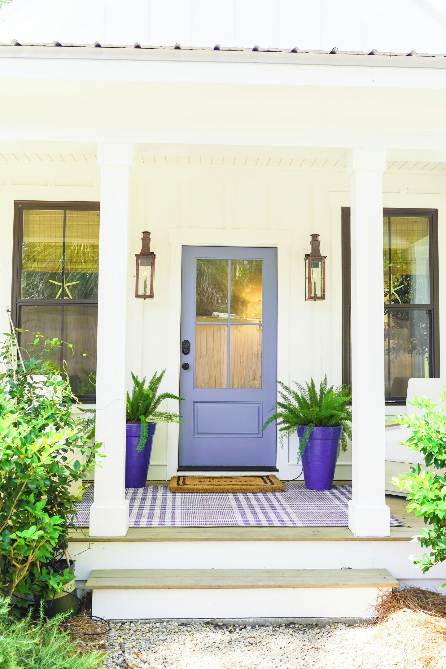 A house with a blue door, two potted plants, and a porch with a checkered mat.