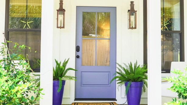 Une maison avec une porte bleue, deux plantes en pot et un porche doté d’un paillasson à carreaux.