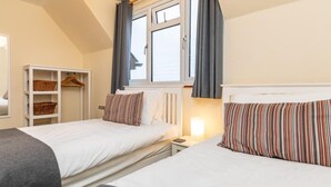 Een slaapkamer met twee bedden, een witte kledingkast en een raam met gordijnen.