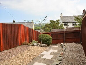 A backyard with a red fence, a stone pathway, and a small bush. - 2 Bed in Boscastle (oc-54474) (Boscastle)
