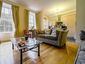 A cozy living room with a sofa, a glass coffee table, and a dining area with a table and chairs. - 1 Bed in Keswick (oc-sz046) (Keswick)