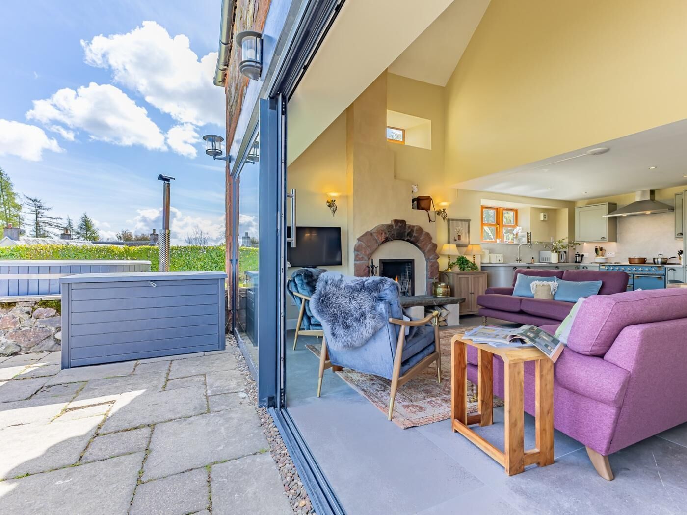 An open-plan living area with a fireplace, a sofa, a coffee table, and a kitchen in the background.