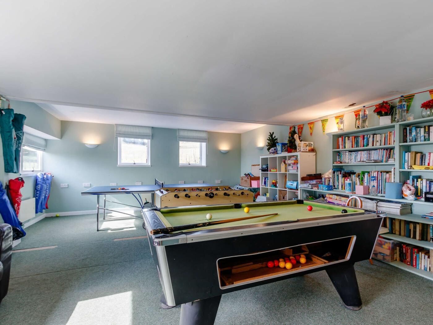 A pool table in a room with a bookshelf and a window.