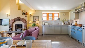 A cozy kitchen with a stone fireplace, a dining area with a table set for two, and a modern kitchen with blue cabinets and a large stove. - 3 Bed in Perth (oc-82831) (Abernyte)
