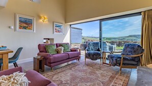 A spacious living area with a large window offering a view of the countryside, a purple sofa, and a dining table with chairs. - 3 Bed in Perth (oc-82831) (Abernyte)