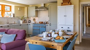 A kitchen with a stove, sink, and cabinets, a dining table with chairs, and a purple sofa. - 3 Bed in Perth (oc-82831) (Abernyte)